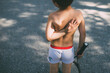© Cavan Images - Rear view of shirtless boy holding tennis racket on road