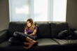 © Cavan Images - Full length of thoughtful girl sitting on sofa by window at home