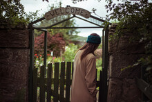 Person Enters Lush Garden Gate With Welcome Sign