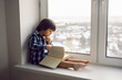 © saulich84 - boy child sits on the window of a house with a book in winter on a high floor