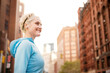 © Cavan Images - Side view of cheerful woman standing against buildings on sunny day