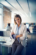 © Cavan Images - Portrait of confident businesswoman with arms crossed leaning on table in office