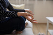 © fizkes - Close up cropped shot of young woman sitting on sofa cross legged in yoga asana. Millennial female practice meditation relaxation exercises on couch at home. Focus on hand fingers joined in mudra sign