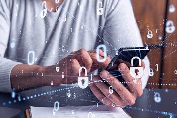 A programmer is browsing the Internet in smart phone to protect a cyber security from hacker attacks and save clients confidential data. Padlock Hologram icons over the typing hands.