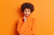 © wayhome.studio  - Serious displeased young African American woman frowns face keeps finger near lips dressed in casual sweater isolated over vivid orange background. Negative emotions and face expressions concept