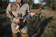 © Cavan Images - Midsection of man loading bullet in rifle on grassy field