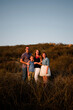 © Cavan Images - Happy family standing together amidst plants on field against sky during sunset