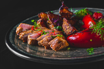 Poster - fried meat with potatoes, pepper, tomatoes, herbs and spices in plate on black wooden table background