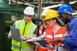 © amorn - Diversity factory worker working with computer laptop in factory. Male and female worker wearing safety uniform, helmet and gloves at work factory. Group of worker working at factory