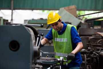 Asian male worker working with lathe machine in factory. Male engineer worker checking, repair or maintenance machine in factory. Male worker wearing safety uniform, helmet and gloves at work factory