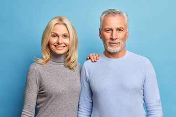 Sticker - Portrait of mature couple stand next to each other look directly at camera have satisfied expressions enjoy time together isolated over blue background. Relationship and family concept. Studio shot