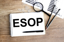 ESOP . Text On White Notepad Paper On Wood Background, Near A Magnifying Glass.