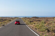 © Cavan Images - Blue cabrio car driving empty paved road in desert volcanic landscape