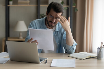 Confused shocked self employed businessman holding paper letter informing about accumulated bank debt unexpected financial problem. Upset stressed young male enterpreneur get loan application rejected