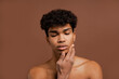 © Ivan - Photo of attractive black man with piercing touches his smooth face. Naked torso, isolated brown color background