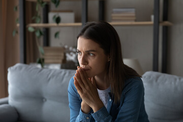 Worried young woman sit on sofa look aside lean forward with folded hands feel fear anxiety. Teen female stressed with unwanted pregnancy thinking on abortion hesitate have doubts making hard decision