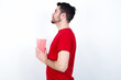 © Roquillo - Young handsome man in red T-shirt against white background eating popcorn looking to side, relax profile pose with natural face with confident smile.