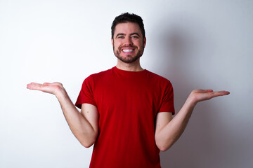 Cheerful cheery optimistic Young handsome man in red T-shirt against white background eating popcorn holding two palms copy space