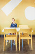 © Cavan Images - Young girl sitting at table and chairs with colorful background