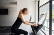 © Cavan Images - Woman riding exercise bike in workout room looking out window