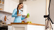 © brillianata - Healthy woman recording her video blog about healthy food additives while standing at kitchen. She is holding a bottle of sports nutrition and smiling