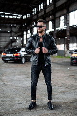 Wall Mural - Stylish handsome man with sunglasses in fashionable clothes stands with the luxury black car on the background. Closeup.