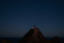 Man With Lantern At The Mountain Top Over Dark Starry Sky.