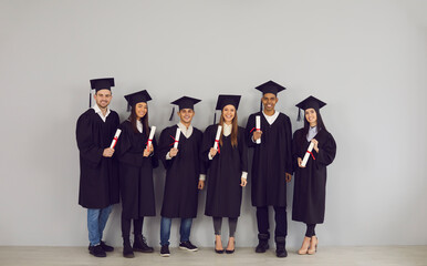 Wall Mural - Group of smiling students multiethnic university graduates standing with diplomas in hands and celebrating in university classroom. Successful graduation from university, education concept