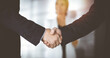 © cameravit - Unknown businesspeople are shaking their hands after signing a contract, while standing together in a sunny modern office, close-up. Business communication, handshake, and marketing concept