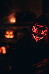 Wall Mural - closeup view of a girl with a red glowing dead mask with a lightsaber next to pumpkins on halloween