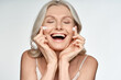 © insta_photos - Happy funny 50s middle aged mature old blond woman applying facial cream on face laughing enjoying skin care beauty spa treatment creme isolated on white background. Mid age skincare concept.