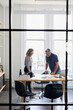 © Cavan Images - Businessman discussing with female colleague in creative office seen through window