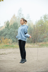 Poster - Blond active young woman in sportswear exercising with skipping-rope on path