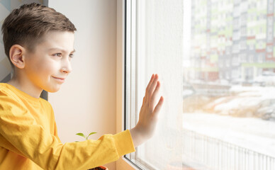 one sad little boy standing near the window at the day time.