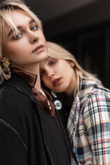 Couple young fashion lesbians in stylish clothes in street. Sexy girl fashion model in black jacket hugs girlfriend checkered wear in street. Homosexuality love and lifestyle relationship concept.