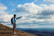 © Cavan Images - Girl with red backpack standing at the mountain top and watching mountain panorama