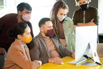 Sticker - Group of young creative designers gathered by table in front of computer monitor