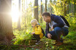 canvas print picture - School boy and his father hiking together and exploring nature with magnifying glass. Child with his dad spend quality family time together in the sunny summer forest.