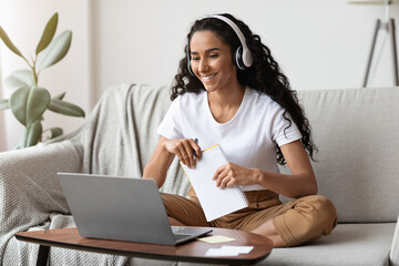 Wall Mural - Cheerful lady attending online course, using laptop and wireless headset