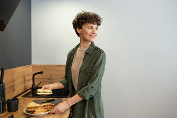 Sticker - Happy young brunette female in casualwear taking plate with homemade sandwiches