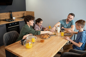 Sticker - Happy family of four enjoying breakfast by served dinner table in the kitchen