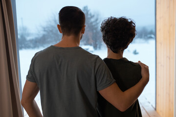 Wall Mural - Rear view of young affectionate relaxed couple standing by large window