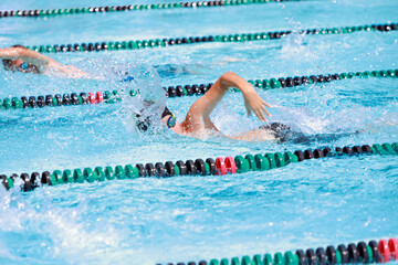 Canvas Print - Motion blurred swimmers in a freestyle race, focus on shoulder and water drops