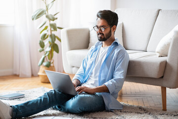 Wall Mural - Home Office. Handsome Eastern Male Freelancer Working With Laptop In Living Room