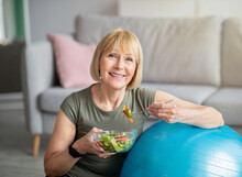 Exercise And Healthy Diet Concept. Senior Woman With Fitball Eating Fresh Vegetable Salad At Home