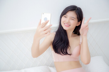 Wall Mural - Beautiful young asian woman sexy in underwear talking a selfie on smartphone for social network in the bedroom, girl in lingerie relax with taking a picture on mobile phone on bed in the bedchamber.