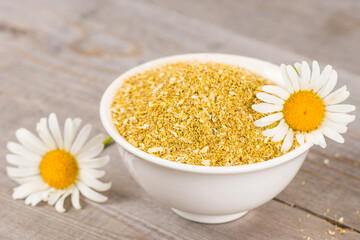 dried chamomile in white bowl and fresh flowers on aged wooden planks