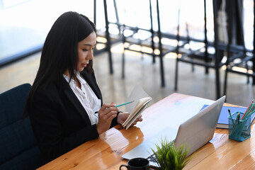 Young businesswoman making note on notebook and working on computer laptop at office.