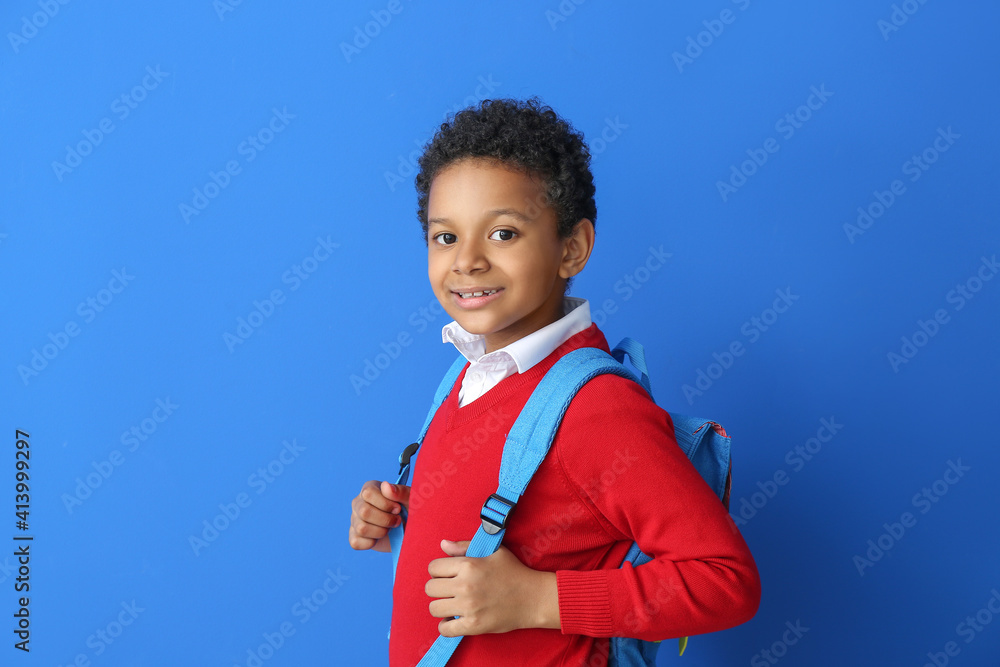 Little African-American schoolboy on color background
