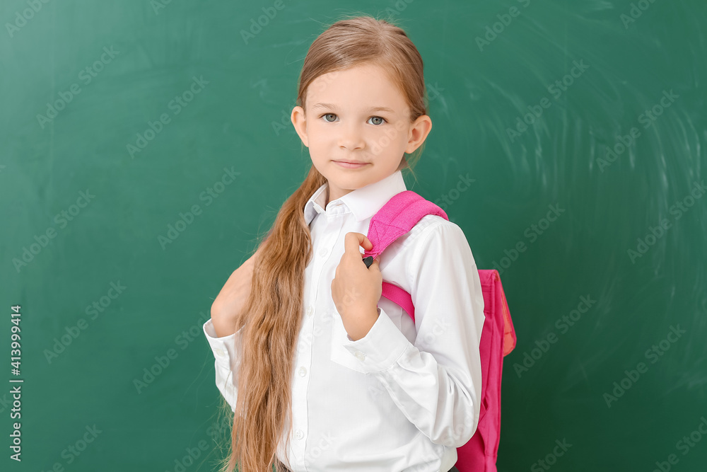 Little schoolgirl near chalkboard in classroom